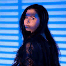 a woman with long black hair is standing in front of a blue wall with a shadow on her face .