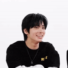 a young man wearing a black shirt and a necklace is smiling and looking at the camera .