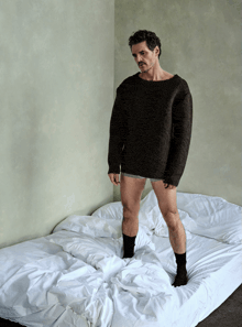 a man in a sweater stands on a bed