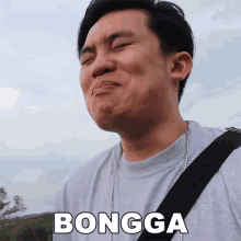 a man wearing a gray shirt and a black strap is making a funny face and the word bongga is above him