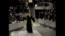 a woman in a long black dress is dancing on a stage in front of a crowd ..