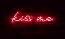 a red neon sign that says `` kiss me '' on a dark brick wall .