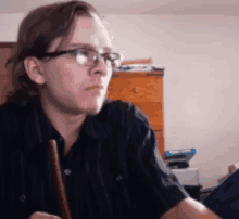 a man wearing glasses and a black shirt is sitting at a desk