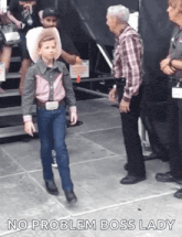 a young boy dressed as a cowboy is walking towards a man in a plaid shirt and tie .