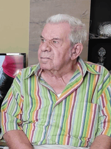 a man wearing a colorful striped shirt sits in front of a tv