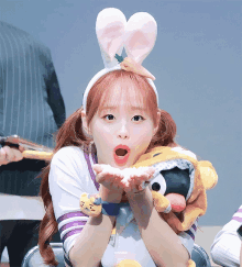 a girl wearing bunny ears holds a stuffed animal and blows a kiss