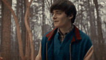 a young man in a blue jacket is standing in the woods .