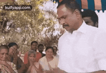 a man in a white shirt is standing in front of a crowd of people and talking to them .