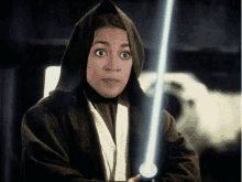 a woman in a hooded robe is holding a light saber in her hand .