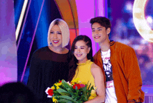 a woman in a yellow top is holding flowers next to two other people