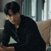 a man sitting on a couch wearing a black jacket