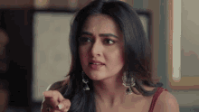 a woman in a red top and earrings is pointing her finger at something .