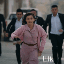 a woman in a pink dress is running with a group of men in suits behind her