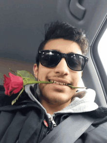 a man wearing sunglasses has a rose in his mouth