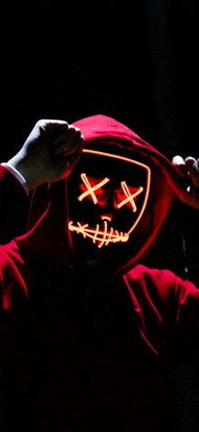 a person in a red hoodie is wearing a neon mask with x 's on it .