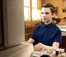 a boy in a blue shirt is typing on a computer