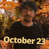 a man wearing glasses stands in front of trees with the date october 23