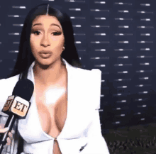 cardi b is talking into a microphone while wearing a plunging white top .