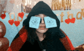 a woman wearing a hooded jacket has a pair of sticky notes on her eyes