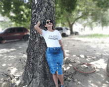 a woman leaning against a tree wearing a gucci t-shirt