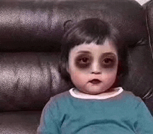 a little girl is sitting on a couch with black circles on her eyes .