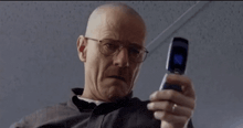 a bald man with glasses is holding a flip phone