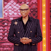 a bald man wearing glasses and a striped suit is standing with his hands folded