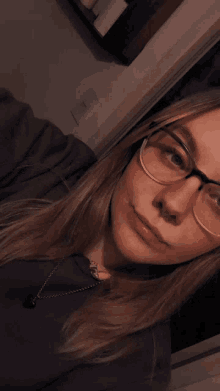 a young woman wearing glasses and a necklace takes a selfie