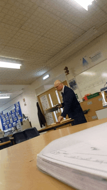 a man in a suit is cutting a piece of wood with a saw in a classroom