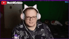 a man wearing a pair of pink cat ears headphones is smiling in front of a green screen that says nerdcrime