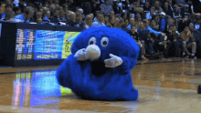 a blue mascot is dancing on a basketball court in front of a crowd that is watching a basketball game