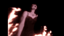 a woman in a black dress is standing in front of a large fire .