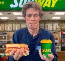 a man is holding a sandwich and a cup of subway