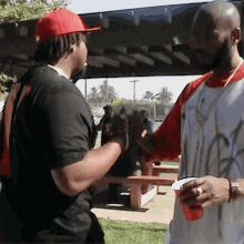 a man wearing a red hat is shaking hands with another man wearing a white shirt with graffiti on it