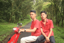 two young men in red shirts are riding a red scooter on a dirt road