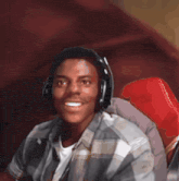 a young man wearing headphones and a plaid shirt is smiling