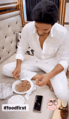 a man in a white shirt is sitting on a couch with a plate of food in front of him and the words #foodfirst below him