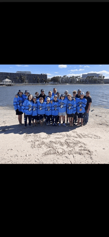 a group of people posing for a picture on a beach with a lake in the background