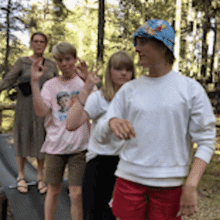 a group of people are standing in the woods and one of them is wearing a hat with flowers on it