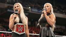 two women are standing in a wrestling ring and one has a w belt on