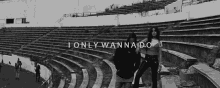 a black and white photo of two women standing in front of a stadium with the words `` i only wanna do '' .