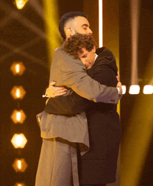 two men hugging each other on a stage with a yellow background