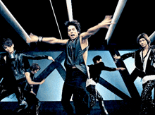 a man in a black vest is dancing with his arms outstretched in front of a group of people