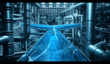 a blue water slide in a factory with pipes and lights