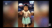 a little girl in a blue skirt stands in front of a sign that says ' chinese ' on it