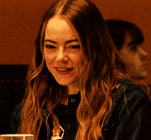 a woman with long brown hair is smiling while sitting at a table with a glass of water in front of her .