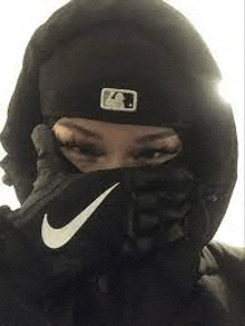 a woman wearing a nike mask and a beanie is covering her face .