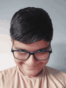 a boy wearing glasses and a tan shirt smiles for the camera