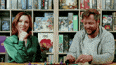 a man and a woman are playing a board game with a box that says tacit