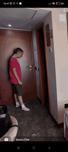 a man in a pink shirt is standing in a hallway next to a door with the time of 18:47